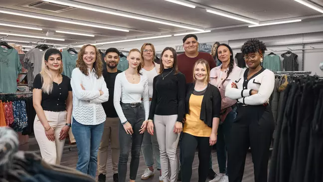 Um grupo de colaboradores encontra-se numa loja, junto a expositores de roupa, a olhar para a câmara.