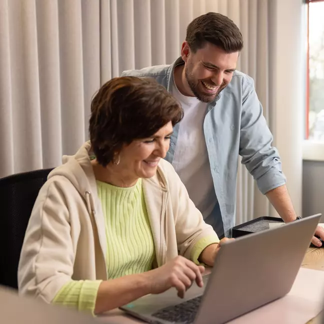Zwei Mitarbeitende lachen gemeinsam vor einem Laptop in einem modernen Büro