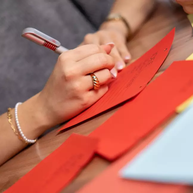 Hände, die etwas auf ein Post-It schreiben mit einem Kugelschreiber