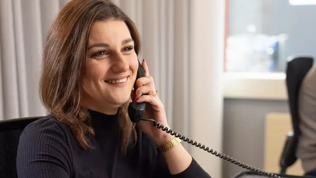 Uma mulher está ao telefone enquanto está sentada no local de trabalho e sorri