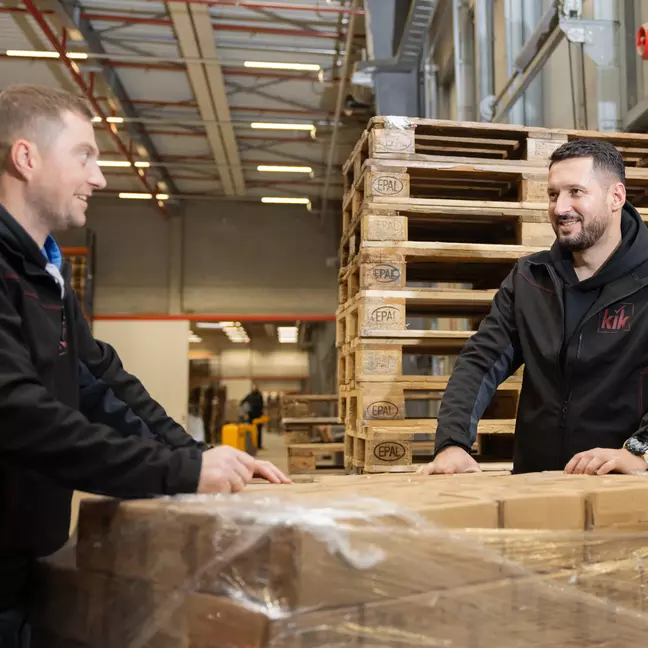 Zwei Lagermitarbeiter packen Ware in einem Lager aus und lächeln