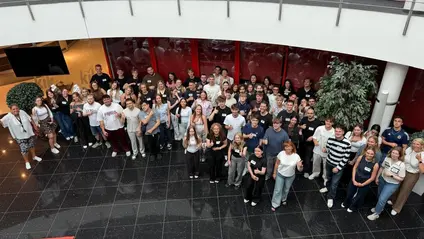 Eine Gruppe von vielen Menschen steht in einem Foyer und schaut nach oben zum Fotoapparat.