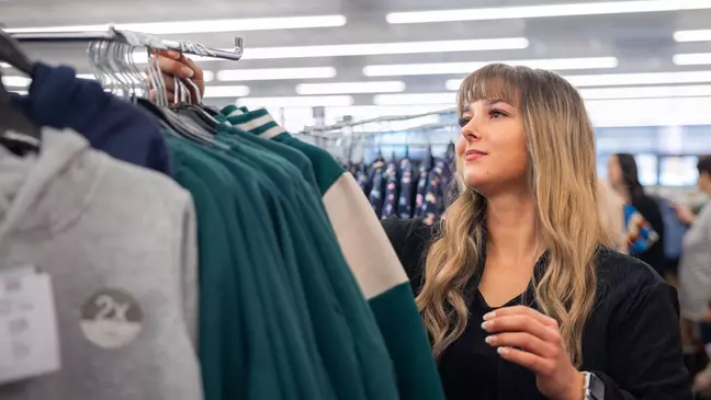 Uma colaboradora organiza artigos têxteis num expositor de roupa