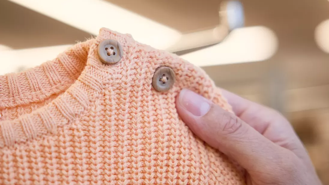 Uma mão segura uma camisola infantil laranja com botões no decote