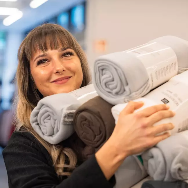 Eine Frau steht lächelnd in einer Filiale und hält viel Ware in den Händen