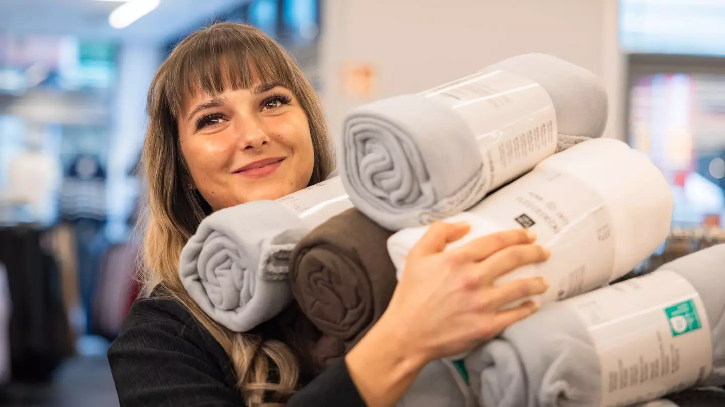 Uma colaboradora apresenta uma seleção de artigos no interior da loja e sorri