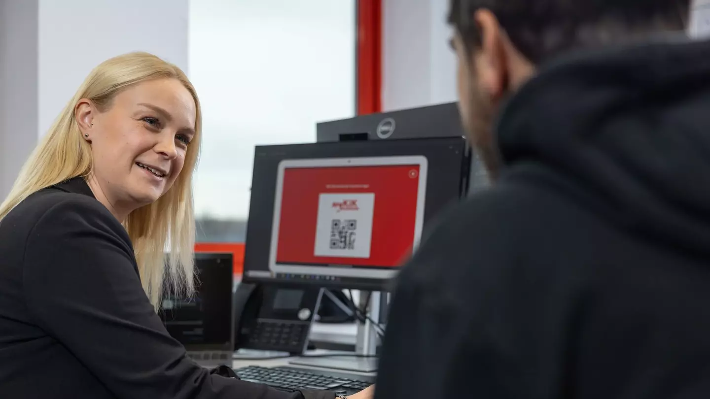 Eine Frau und ein Mann sitzen vor einem Computer, die Frau lächelt und wendet sich dem Mann zu
