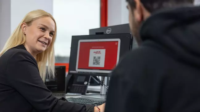 Eine Frau und ein Mann sitzen vor einem Computer, die Frau lächelt und wendet sich dem Mann zu