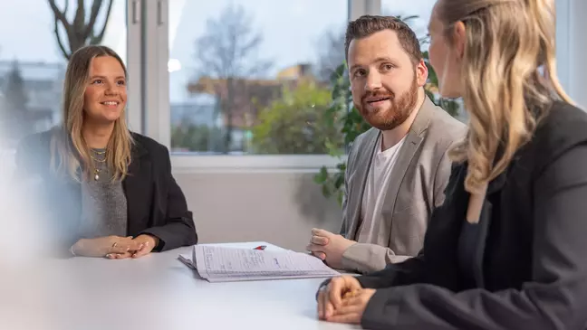 Três colaboradores estão sentados à mesa e trocam ideias durante uma conversa.