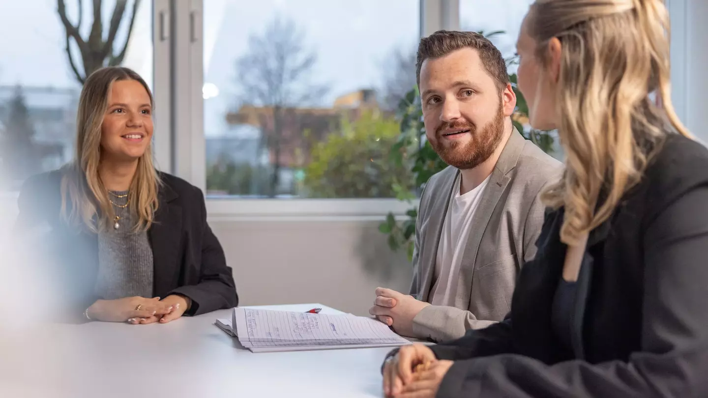 Três pessoas participam numa entrevista de emprego num escritório moderno.