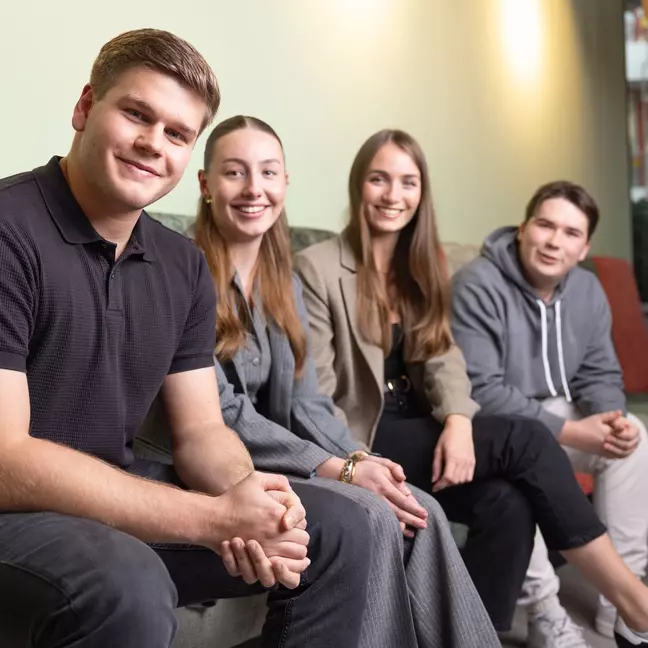 Vier Mitarbeitende sitzen in einer Lounge und lächeln in die Kamera